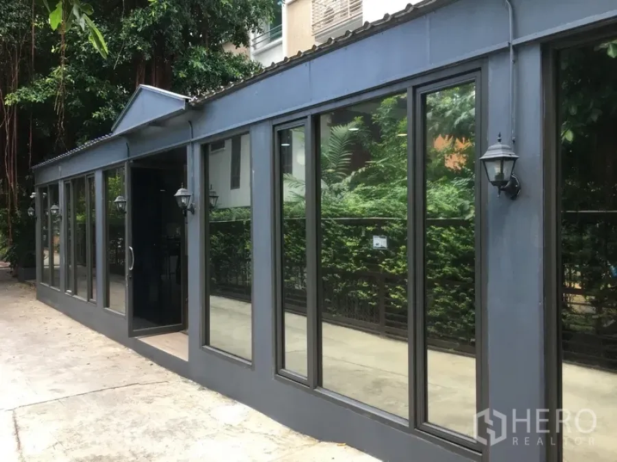 Retail Space for rent in Watthana, Bangkok - Street-facing single-storey retail unit with dark metal facade and large glass windows beside lush greenery in the Thonglor area of Watthana, Bangkok.