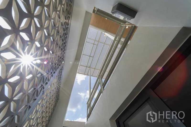 Townhouse for rent or sale in Watthana, Bangkok - Upward view of perforated facade panels with sunlight and sky.