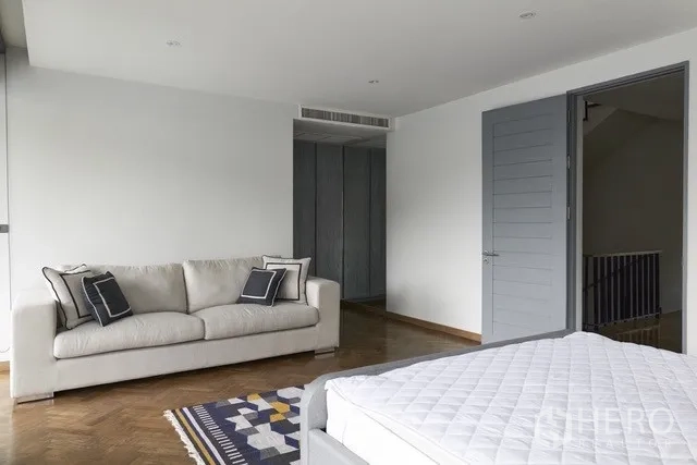 Townhouse for sale in Watthana, Bangkok - Spacious bedroom with a sofa, built-in wardrobes and parquet flooring.