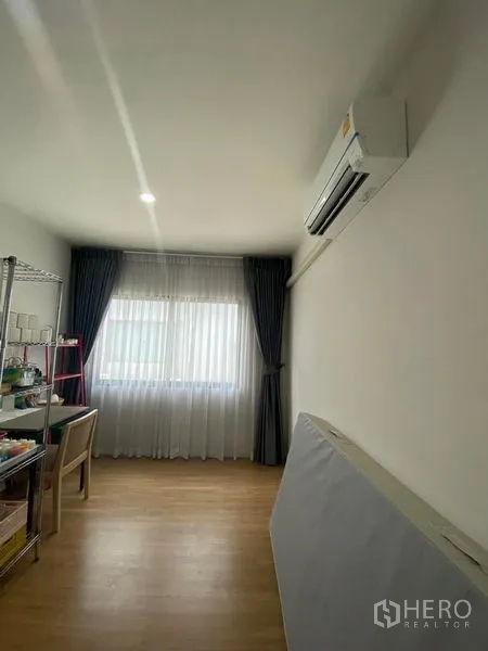 Townhouse for rent or sale in Saphan Sung, Bangkok - Bright room with wood flooring, wall-mounted air conditioner and a window with sheer and blackout curtains.
