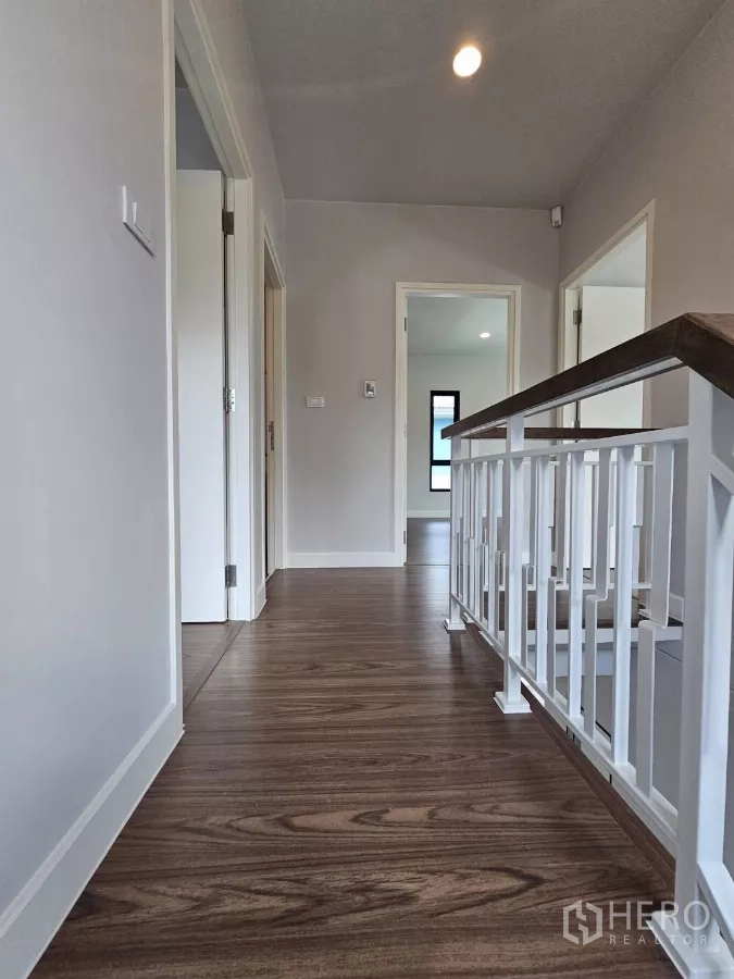 Detached House for sale in Lam Luk Ka, Pathum Thani - Upper hallway with wood laminate floors and white railing.