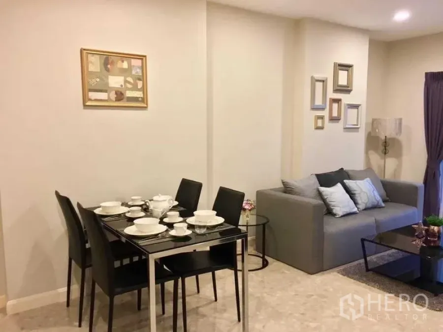 Condominium for rent in Khlong Toei, Bangkok - Dining and living space set with tableware and a gray sofa in warm tones.