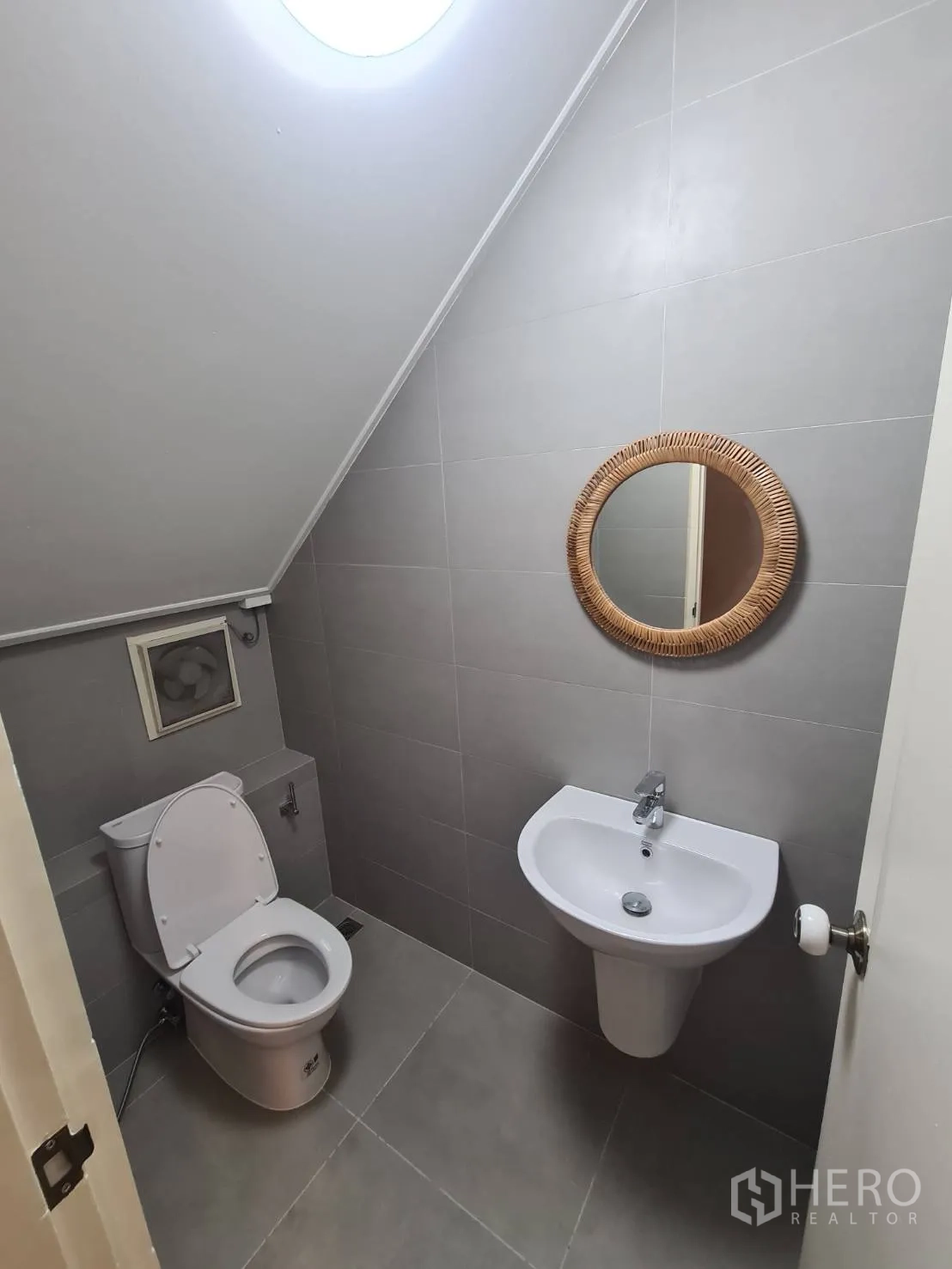 Detached House for rent in Khlong Toei, Bangkok - Compact guest toilet with gray tiles, round mirror and skylight.