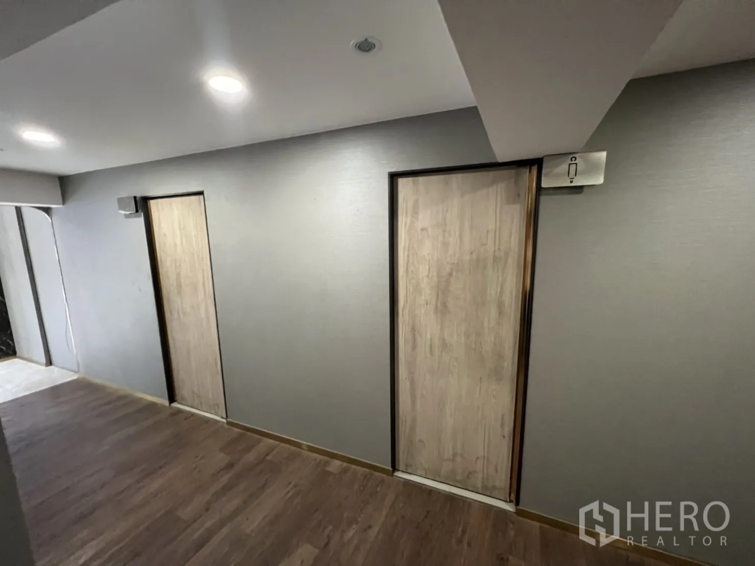 Shophouse for rent in Phra Khanong, Bangkok - Corridor with two restroom doors and wood flooring under recessed lights.