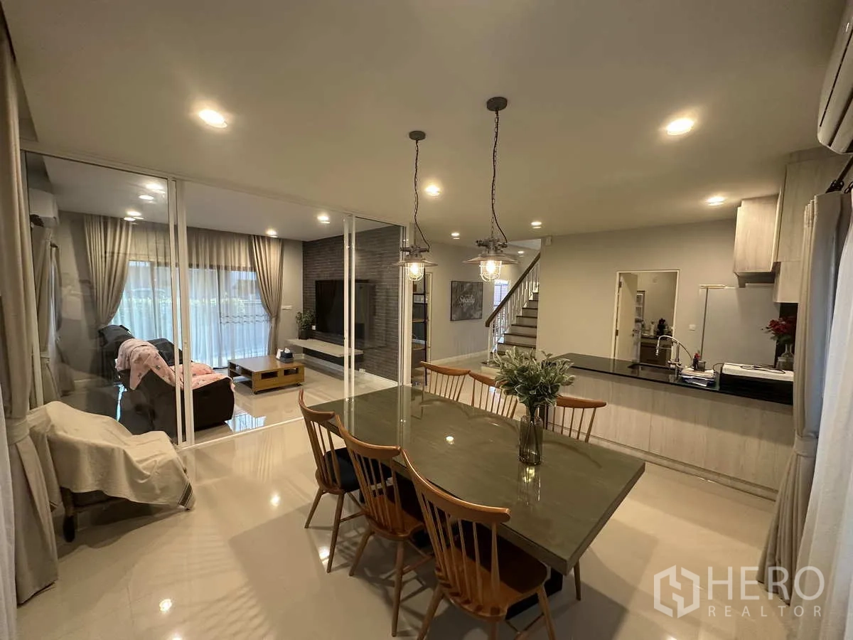 Detached House for rent or sale in Lam Luk Ka, Pathum Thani - Spacious dining room with pendant lights overlooking the living area through glass.