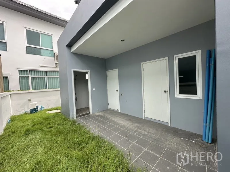 Detached House for sale in Lam Luk Ka, Pathum Thani - Backyard utility area with tiled terrace, service doors and grassy side yard.