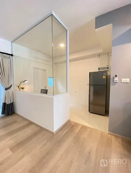 Townhouse for rent in Bang Phli, Samut Prakan - Hallway with glass partition revealing a study desk and view toward the kitchen with fridge.