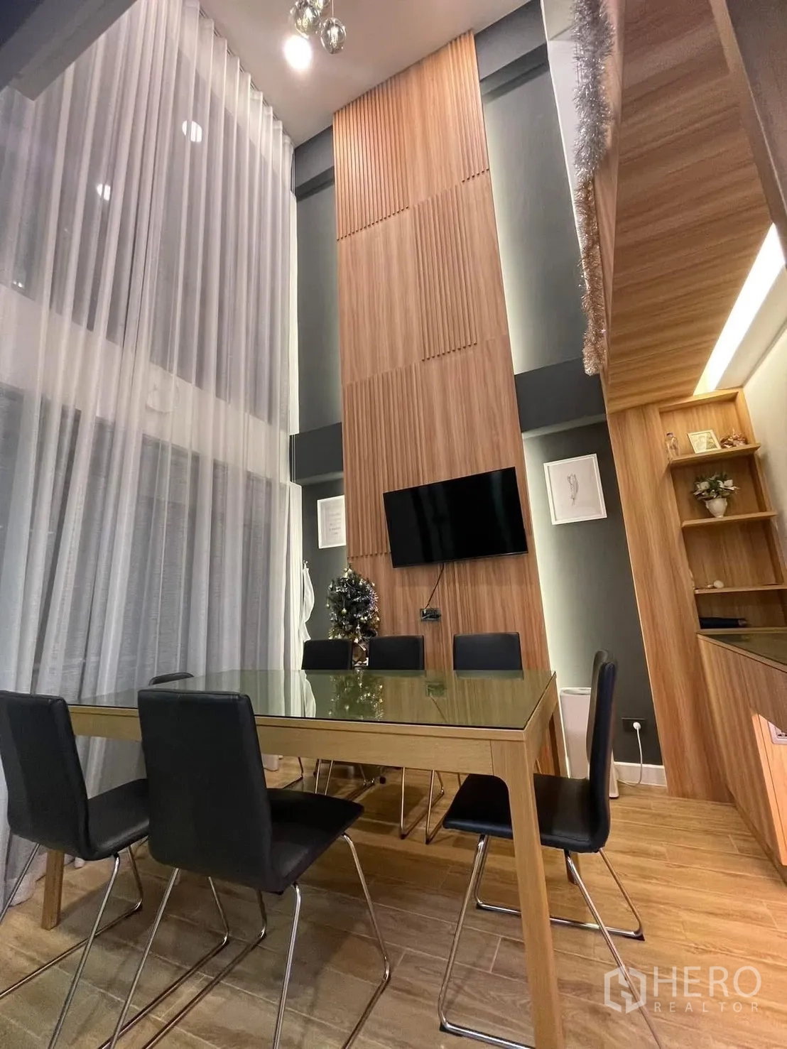 Home Office for rent or sale in Bang Kapi, Bangkok - Double-height meeting and dining area with glass table, wood feature wall, TV and sheer curtains.