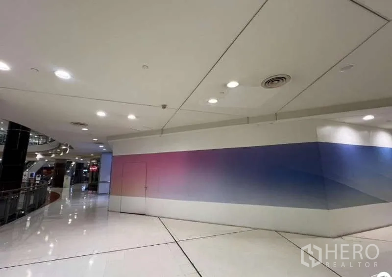 Retail Space for rent - Corner retail unit inside a modern mall corridor with glossy white floors, drop ceiling and recessed lights, offering a long branding wall.
