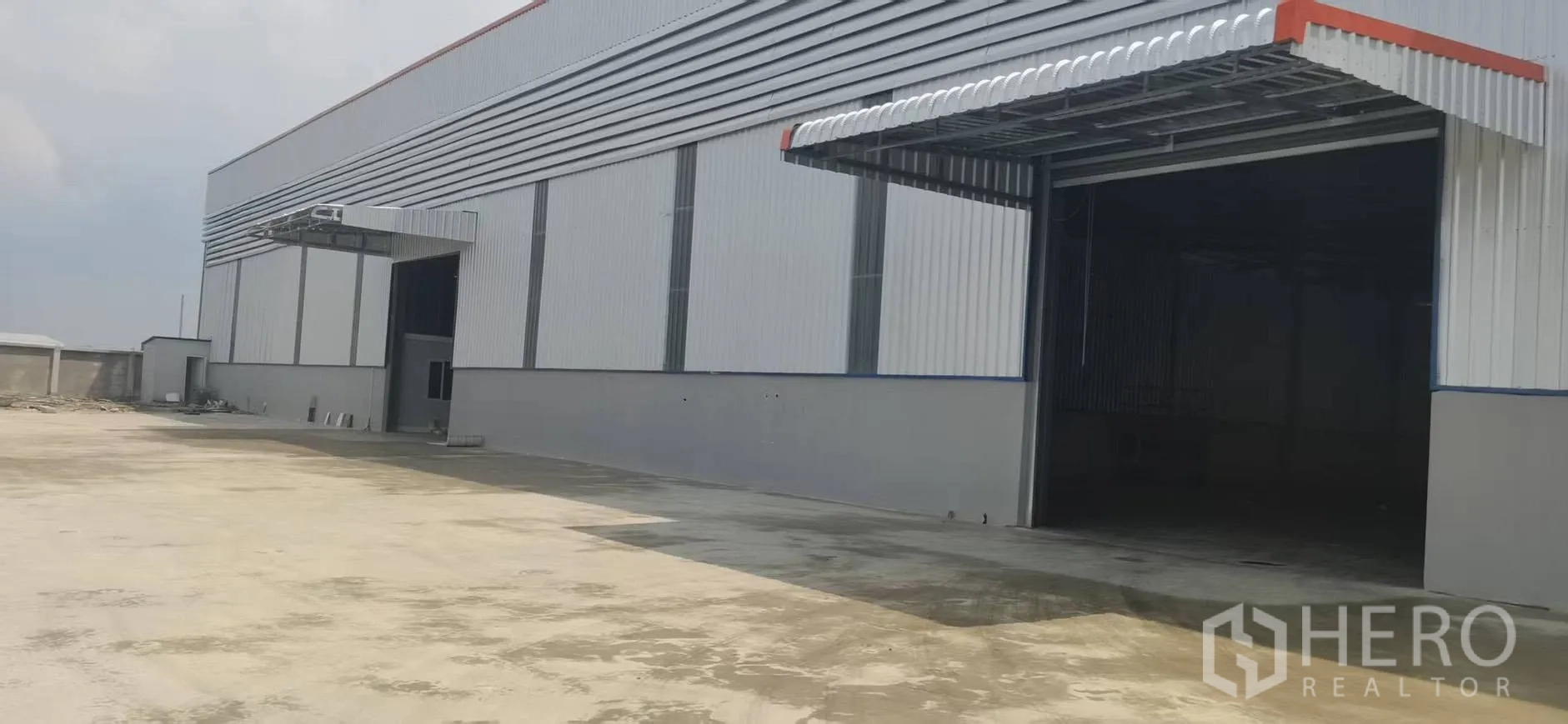 Warehouse for rent in Bang Phli, Samut Prakan - Warehouse exterior with wide roller shutter entrance, covered loading canopy, and large concrete yard.