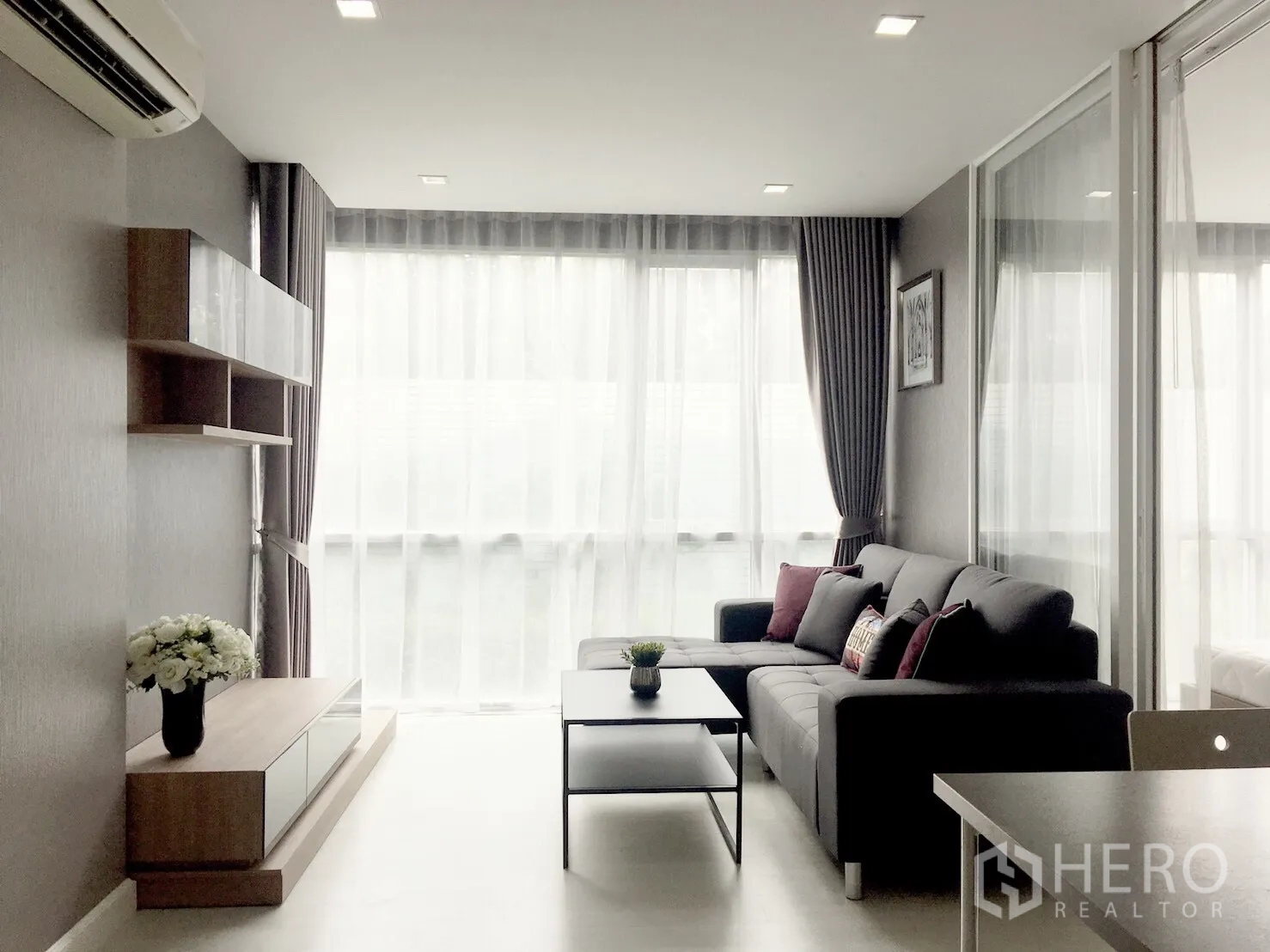 Condominium for sale in Phra Khanong, Bangkok - Bright living room with floor-to-ceiling windows, L-shaped sofa, built-in shelving and a coffee table.