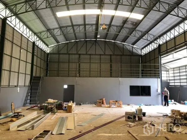 Warehouse for rent in Lam Luk Ka, Pathum Thani - Spacious warehouse interior showing mezzanine platform, stairs, concrete floor and large sliding entrance.