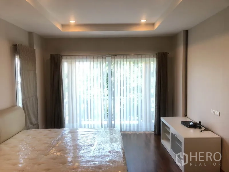 Detached House for rent or sale in Pak Kret, Nonthaburi - Master bedroom with balcony access, sheer curtains and wooden flooring.