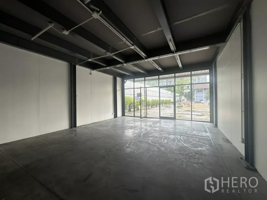 Retail Space for rent - Open-plan retail interior with concrete flooring, floor-to-ceiling front windows, and exposed ceiling beams.
