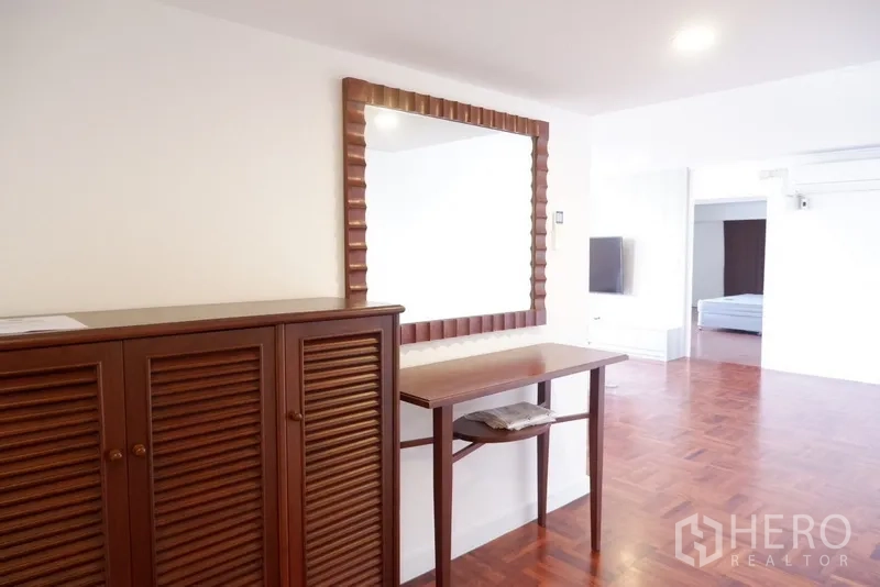 Condominium for rent in Khlong Toei, Bangkok - Close-up of wooden louver cabinet and console with mirror near bedroom entrance.