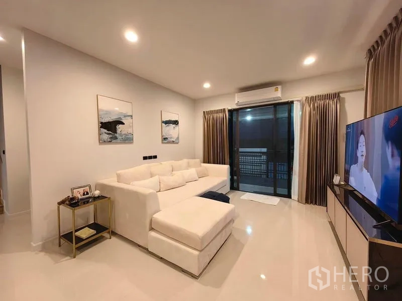 Detached House for rent in Bang Kapi, Bangkok - Cozy living room with L-shaped white sofa, sliding glass doors and TV console