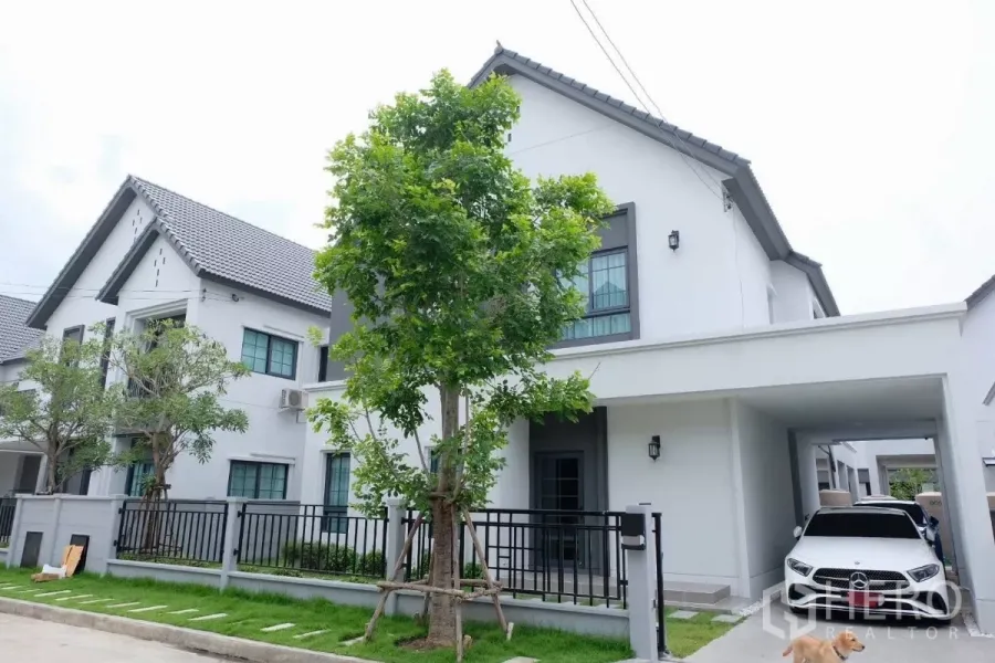 Detached House for sale in Bang Phli, Samut Prakan - Modern two-storey detached house with carport, black fence, front lawn and shade trees on a quiet residential street