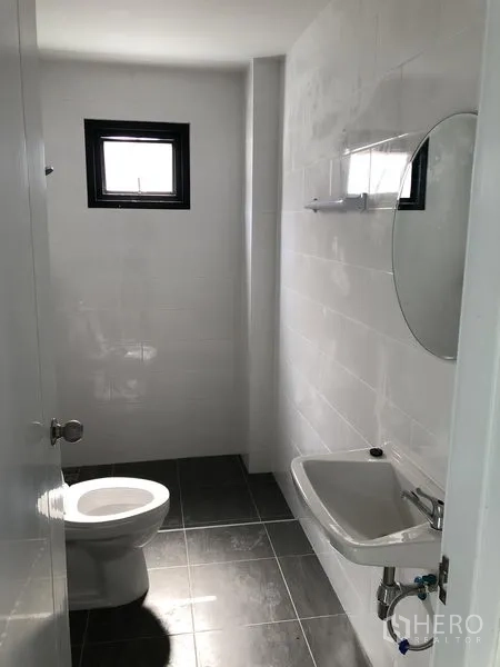 Factory for rent in Bang Yai, Nonthaburi - Simple tiled bathroom with a toilet, sink, mirror and ventilation window.