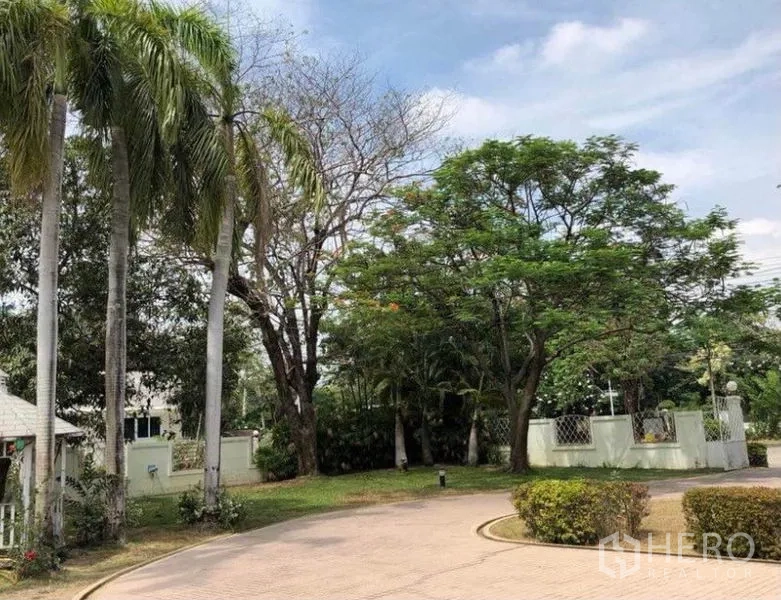 Detached House for sale in Mueang Samut Prakan, Samut Prakan - Curved driveway bordered by tall palms and mature trees near the gated entrance.