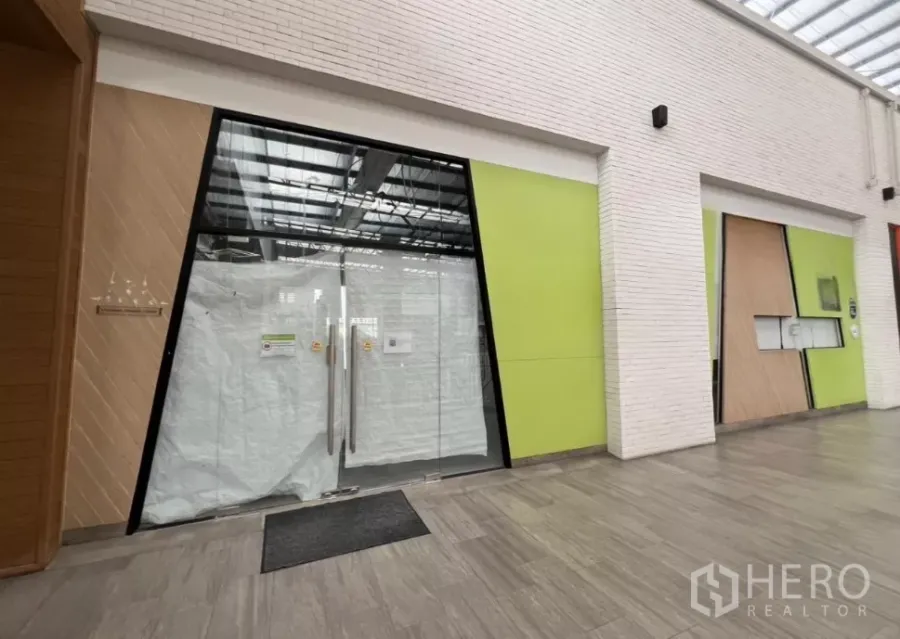 Retail Space for rent in Khlong Toei, Bangkok - Community mall corridor with modern storefront featuring wide glass double doors and lime-green panels.