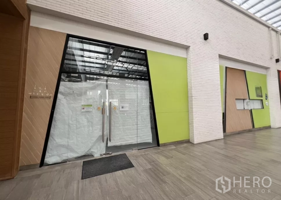 Retail Space for rent in Khlong Toei, Bangkok - Community mall corridor with modern storefront featuring wide glass double doors and lime-green panels.