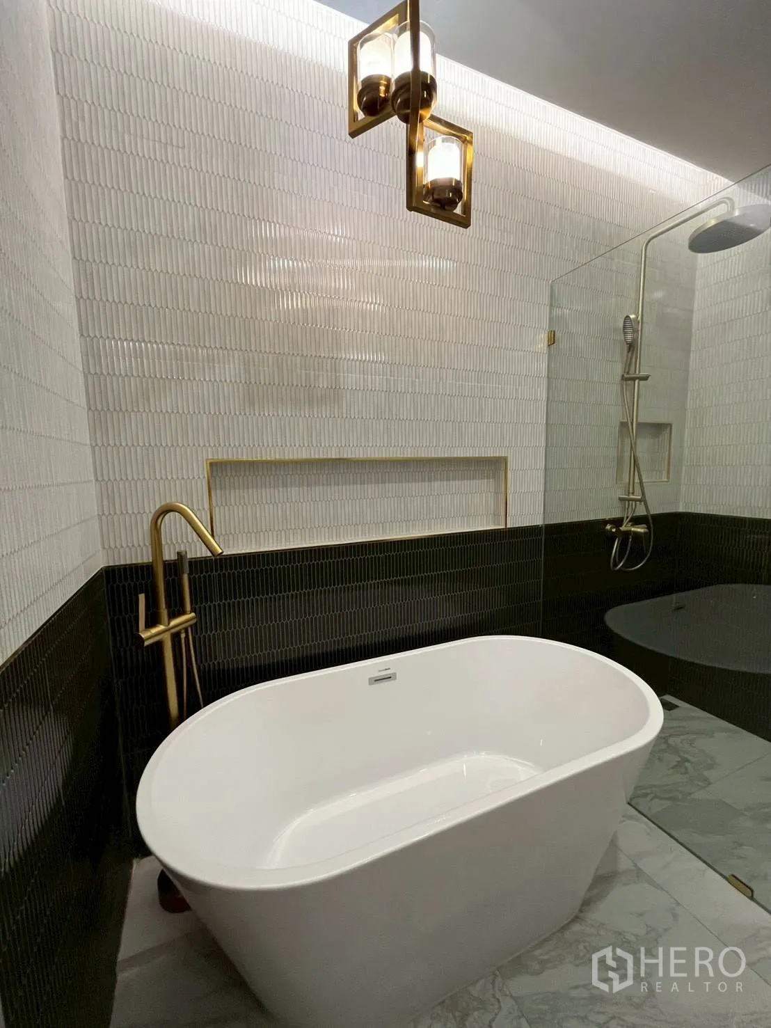 Townhouse for rent in Khlong Toei, Bangkok - Modern bathroom with freestanding tub, gold fixtures, glass shower, and textured tiles.