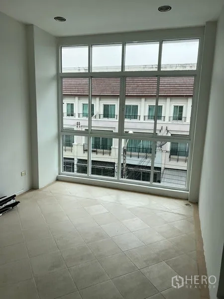 Townhouse for rent in Saphan Sung, Bangkok - Sunlit multipurpose room with floor-to-ceiling windows overlooking neighboring townhouses.