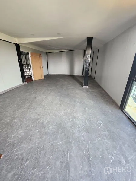Warehouse for rent or sale in Lam Luk Ka, Pathum Thani - Open-plan office floor with gray flooring, black steel columns, large windows and a wooden door.