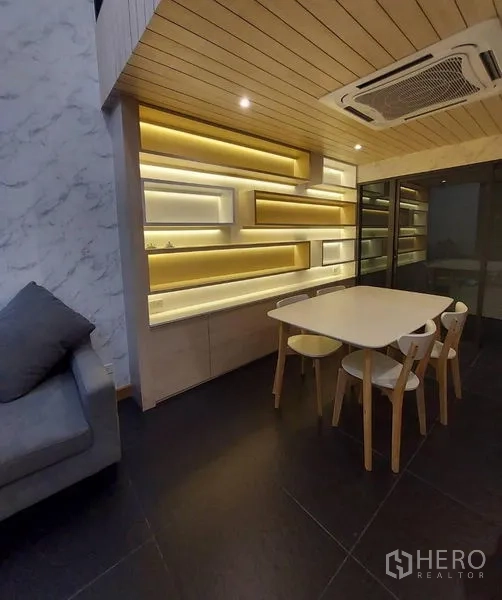 Townhouse for rent in Thanyaburi, Pathum Thani - Dining nook with backlit geometric shelves, white table and wooden chairs under a wood ceiling and cassette AC.