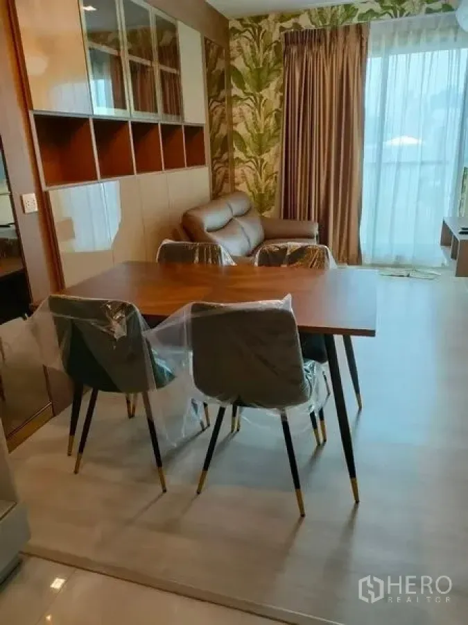 Condominium for rent in Pathum Wan, Bangkok - Open-plan living and dining space with pendant light, sofa and balcony framed by tall curtains.