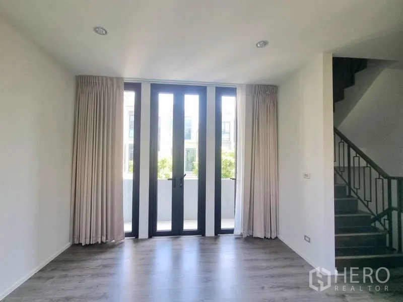 Detached House for rent - Living area with tall glass doors opening to a balcony and a staircase to the side.