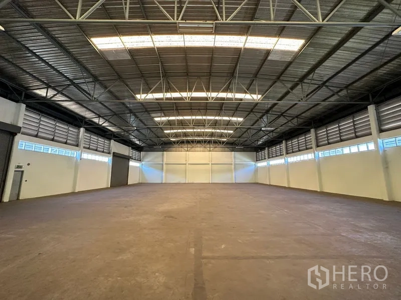 Factory for rent in Chon Buri - Wide-span warehouse interior showing steel roof structure, side windows, and unobstructed floor space.