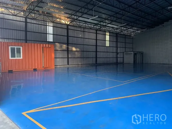 Warehouse for rent in Bang Kapi, Bangkok - Warehouse interior with blue epoxy flooring and an orange container office along the wall.