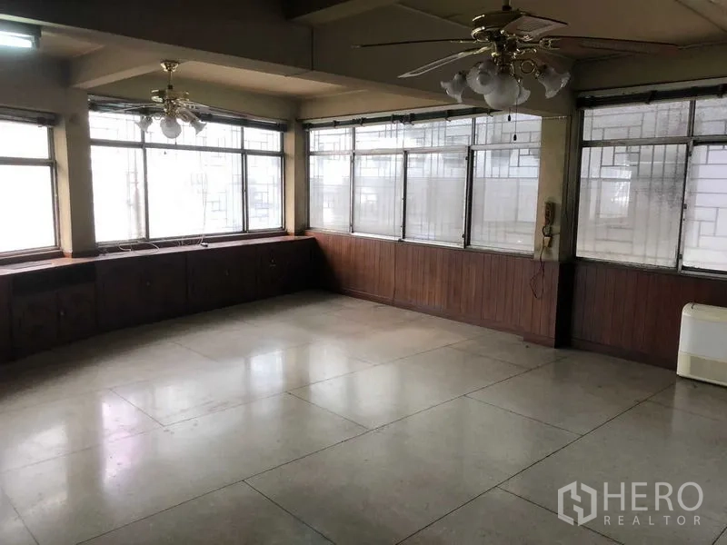 店屋 出租在Khlong Toei, Bangkok - 宽敞的高层房间，环绕窗户与吊扇，木质矮柜沿墙。