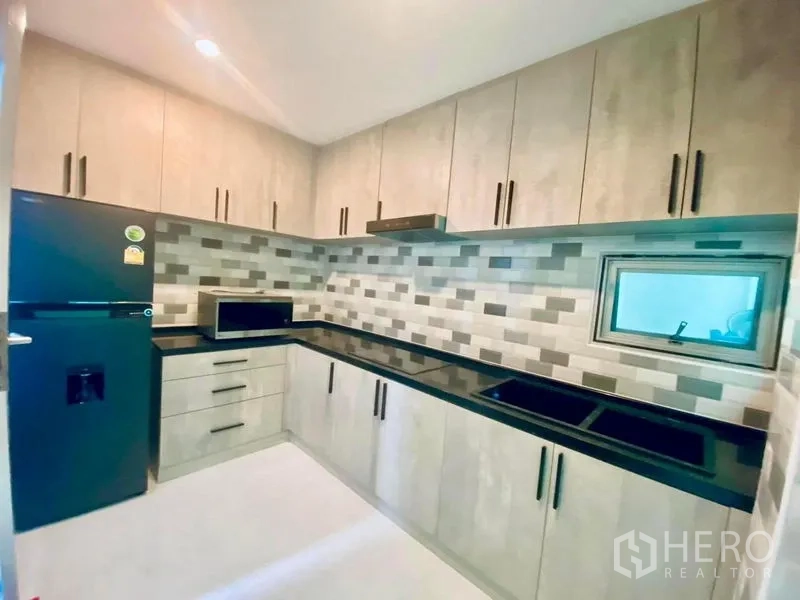 Detached House for rent in Suan Luang, Bangkok - Modern kitchen with ample cabinetry, black countertops and tiled backsplash.