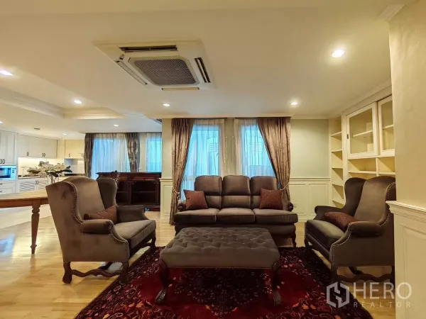 Condominium for rent in Pathum Wan, Bangkok - Cozy seating corner with classic sofa set, tufted ottoman on a red rug and window drapes.
