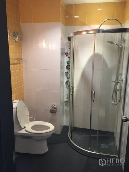 Condominium for rent in Khlong Toei, Bangkok - Guest bathroom with curved glass shower cabin and yellow-white tiles.