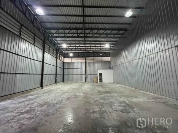 Warehouse for rent in Bang Phli, Samut Prakan - Open storage hall with concrete floor, steel trusses and a small utility room at the rear.