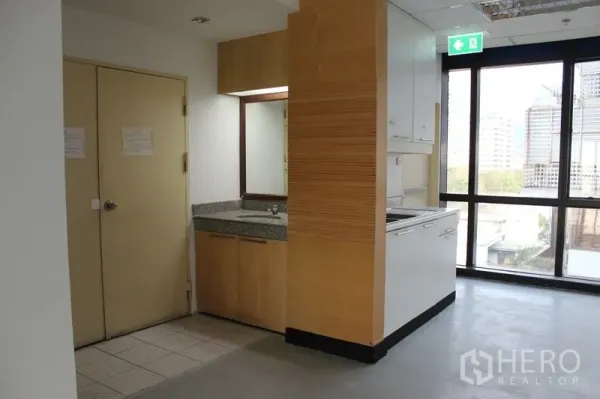 Office Space for rent in Watthana, Bangkok - Pantry nook with sink, stone countertop, and cabinets beside large windows.
