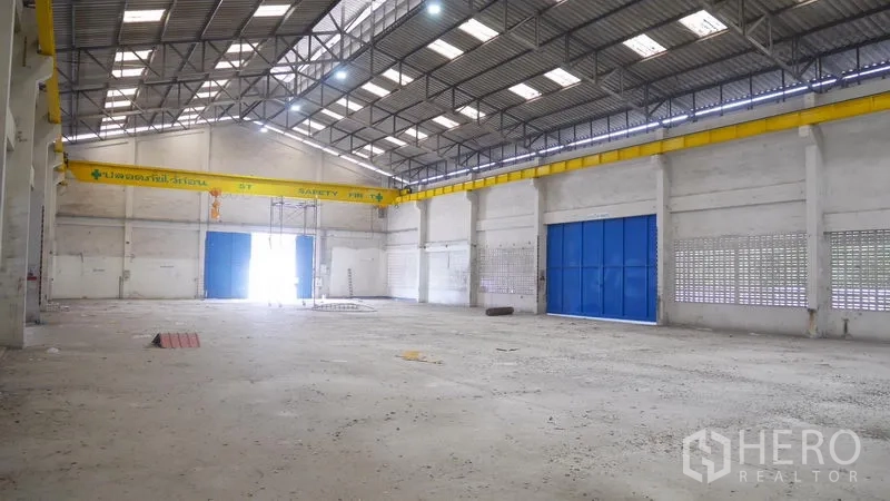 Factory for rent in Khlong Sam Wa, Bangkok - High-clearance warehouse interior with skylights, steel trusses and large blue sliding doors.