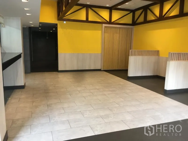 Retail Space for rent in Khlong Toei, Bangkok - Wide view of the main floor showing a tiled central area, feature wall, and slatted doorway.