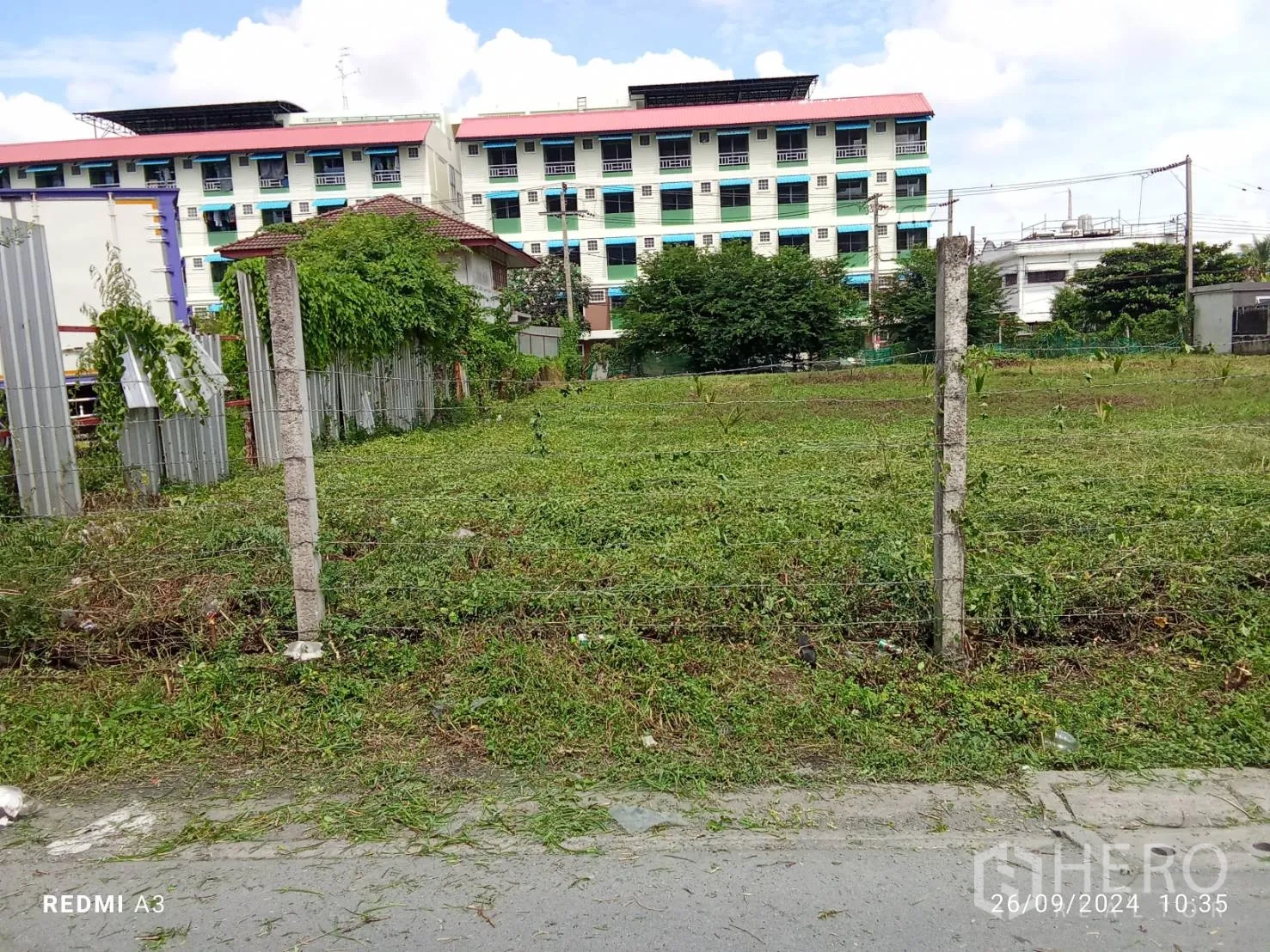 地 出租在Khan Na Yao, Bangkok - 铁丝网围起的平整绿地，面向当地道路与公寓楼。