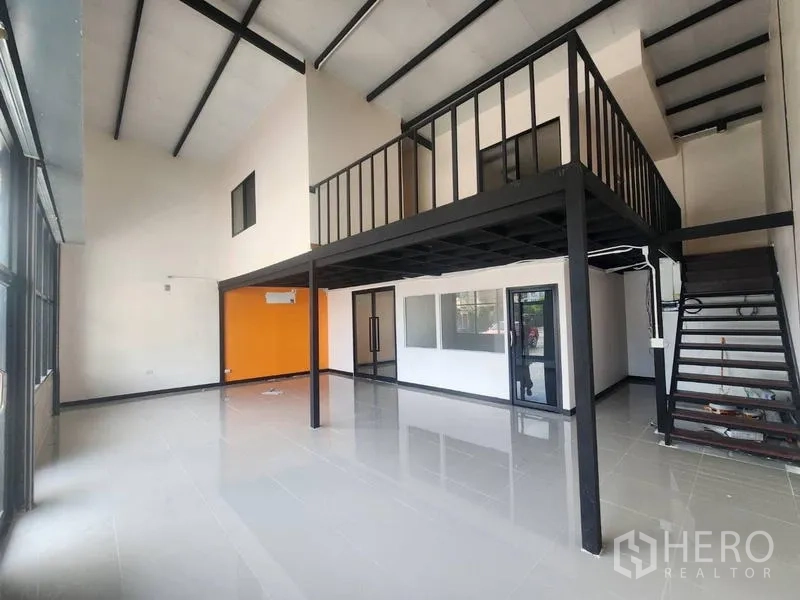 Warehouse for rent in Suan Luang, Bangkok - Double-height main hall with a steel mezzanine and an orange feature wall.