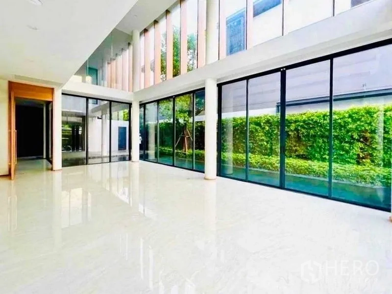 Detached House for sale in Huai Khwang, Bangkok - Expansive glass-walled living room with soaring ceiling and views to the landscaped hedge.