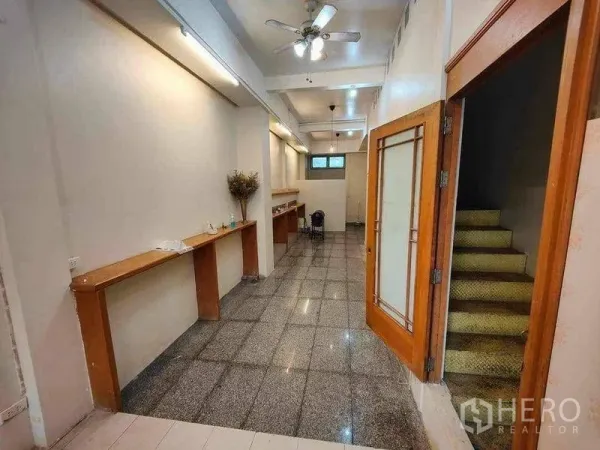 Retail Space for rent in Khlong Toei, Bangkok - Narrow shop interior with granite flooring, wooden built-in counters and a staircase behind a glass door.