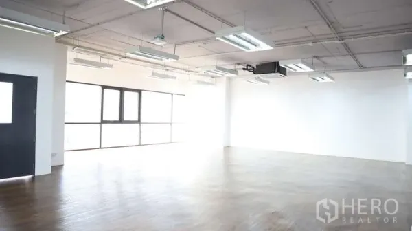Office Space for rent - Spacious office floor with exposed ceiling, multiple LED light panels, and wide window wall.