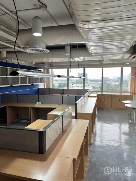 Office Space for rent in Khlong Toei, Bangkok - Row of workstations and storage facing full-height windows with city skyline views.