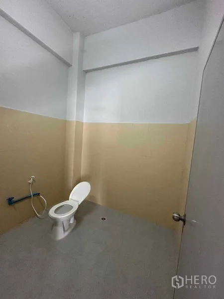 Warehouse for rent in Mueang Samut Sakhon, Samut Sakhon - Simple restroom with toilet, half-height beige wall tiles, and floor drain.