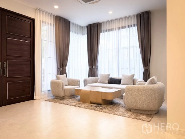 Detached House for rent in Bang Khen, Bangkok - Bright living room with sheer floor-to-ceiling curtains, cozy sofa set and wood entrance door.