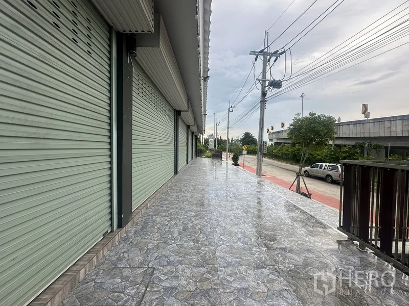 Standalone for rent in Prawet, Bangkok - Covered sidewalk with roll-up shutters along the roadside.